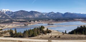 A forest and lake in the distance with mountain peaks in the background on a sunny day, managed by Wildlands Eco-Forestry Inc. for wildfire protection and forest management.